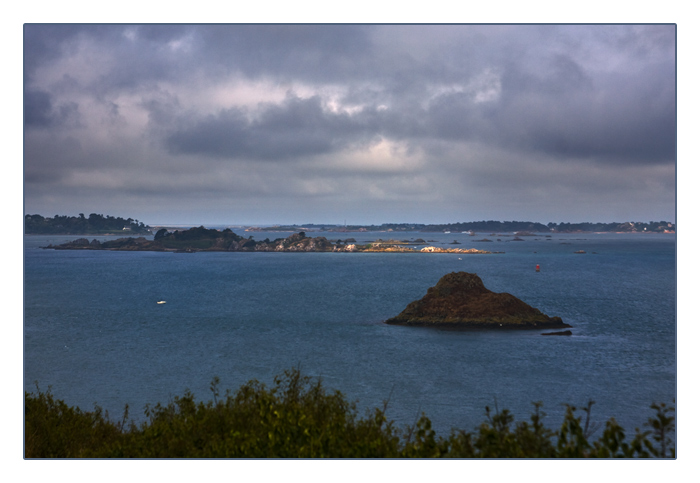 ein Sonnenstrahl fällt durch die dunklen Wolken kurz auf die Insel Île St-Rion, Pointe de Bilfot, Plouézec
